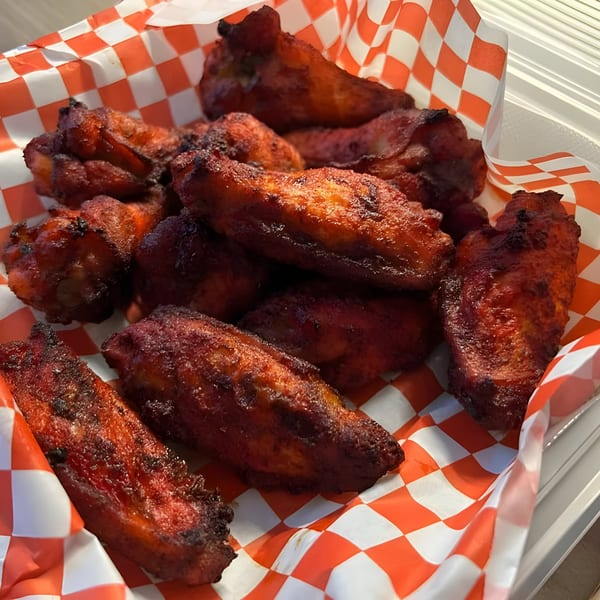 Close-up of Mighty Munch Mtn Curry Pizza's red-hued chicken wings in a red and white checkered paper.