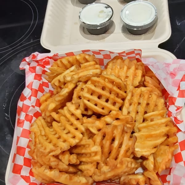 Waffle fries in a red and white checkered paper-lined container with two dipping sauces.