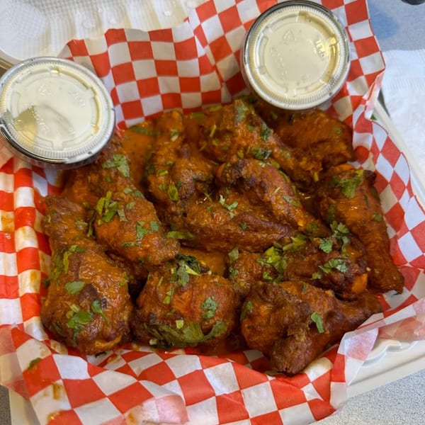 Curry chicken wings with cilantro and two dipping sauces in a red and white checkered basket.