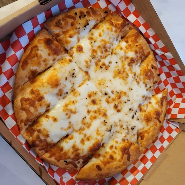 A Mighty Munch Mtn Curry Pizza cheese pizza, cut into slices, in a delivery box with red and white checkered paper.