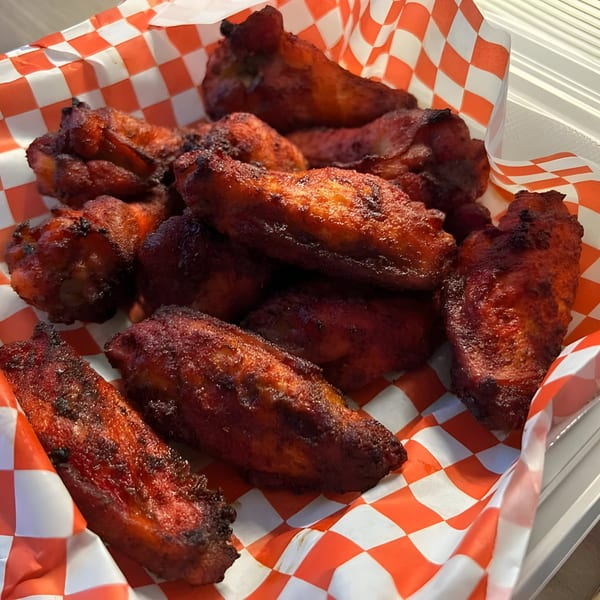 Close-up of Mighty Munch Mtn Curry Pizza's red-spiced chicken wings in a red and white checkered basket.