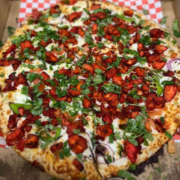 A Mighty Munch Mtn Curry Pizza, topped with red chicken, green peppers, onions, and cilantro.