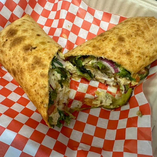 A Mighty Munch Mtn Curry Pizza wrap, cut in half, revealing chicken, lettuce, red onion, and sauce.