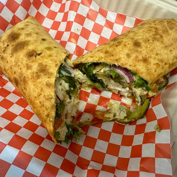 Mighty Munch Mtn Curry Pizza's chicken wrap, cut in half, revealing chicken, lettuce, onions, and sauce.