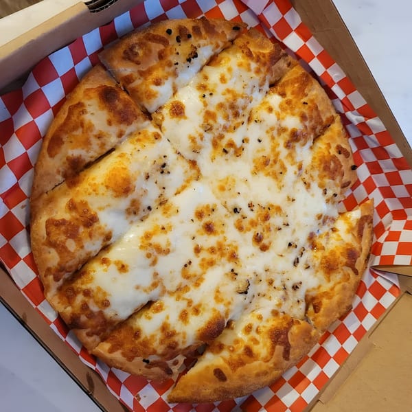Mighty Munch Mtn Curry Pizza's cheese pizza, cut into slices, in a box with red and white checkered paper.