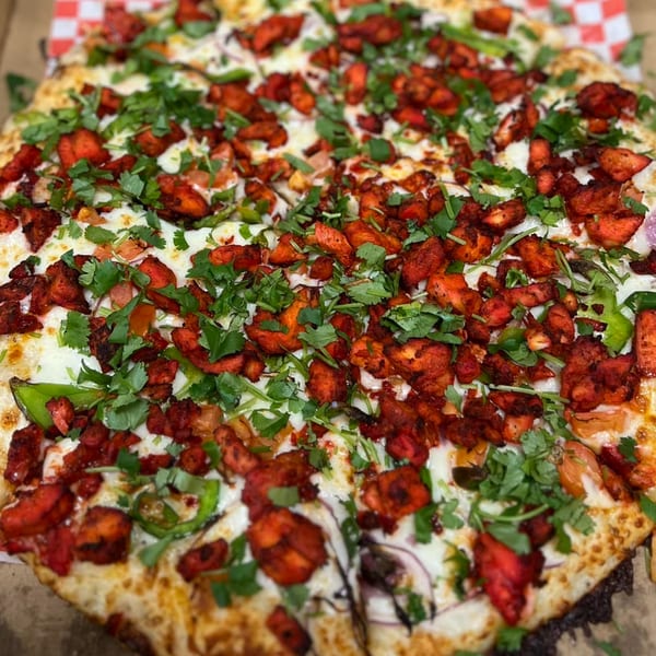 A close-up of a Mighty Munch Mtn Curry Pizza, topped with chicken tikka, green peppers, and cilantro.