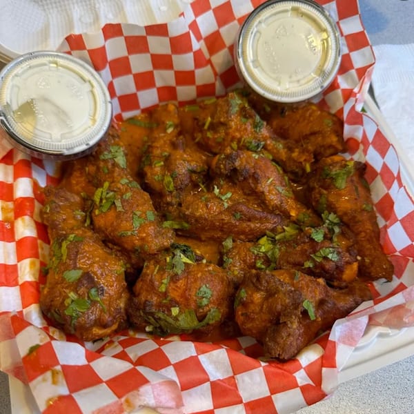 Mighty Munch Mtn Curry Pizza's chicken wings with sauce and cilantro, served with two dipping cups.