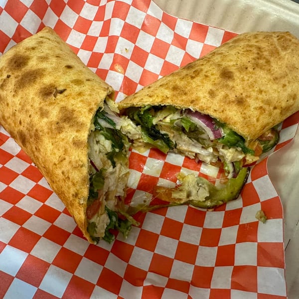 A Mighty Munch Mtn Curry Pizza wrap, cut in half, revealing chicken, lettuce, and red onion.