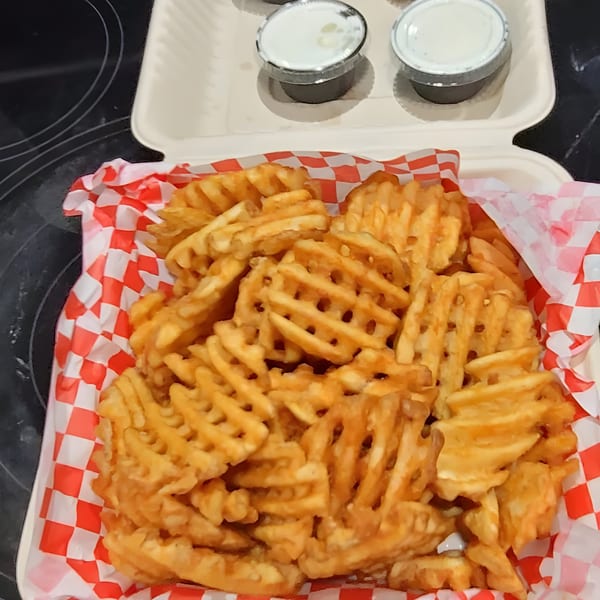 A takeout container filled with golden waffle fries and two small cups of dipping sauce.