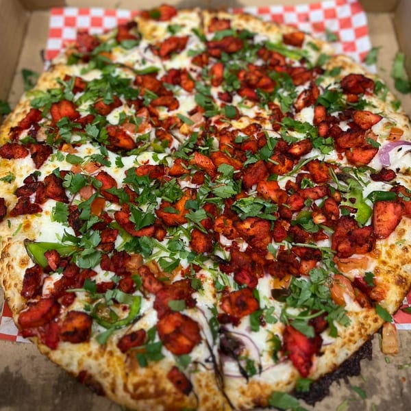 A Mighty Munch Mtn Curry Pizza, topped with vibrant red chicken tikka, green peppers, and fresh cilantro.