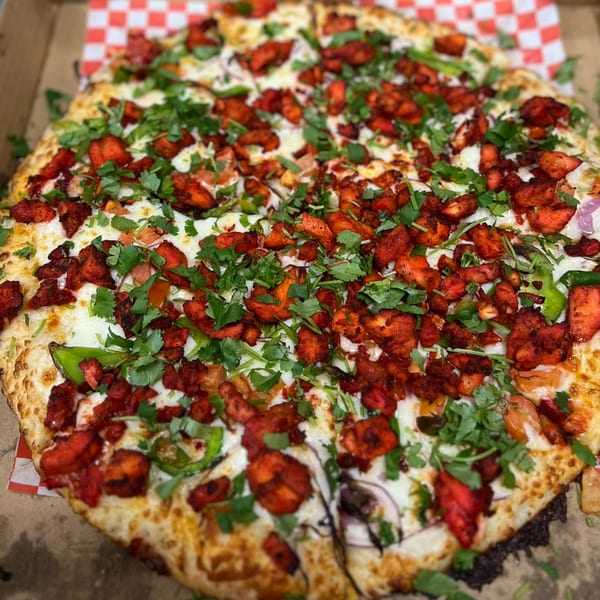 A Mighty Munch Mtn Curry Pizza, topped with red chicken tikka, green peppers, and cilantro.