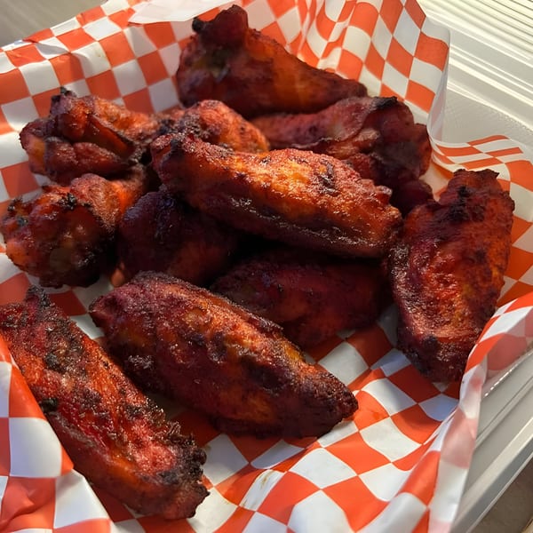 A close-up of Mighty Munch Mtn Curry Pizza's red-hued chicken wings in a red and white checkered paper.