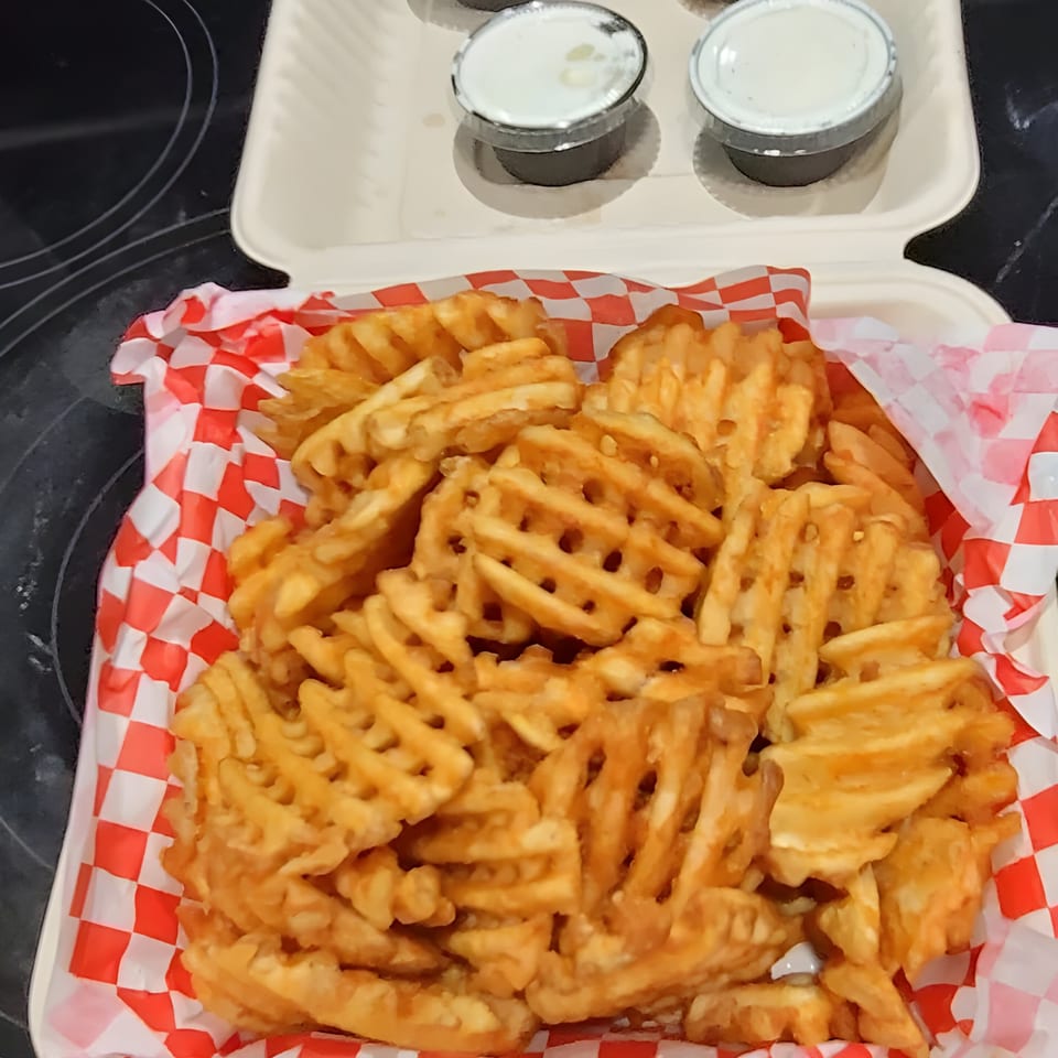 A takeout container filled with golden waffle fries and two small cups of dipping sauce.