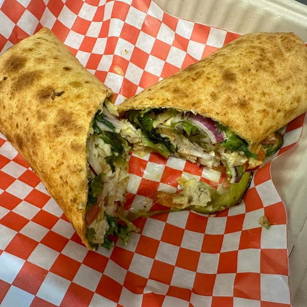 A Mighty Munch Mtn Curry Pizza wrap, cut in half, revealing chicken, lettuce, and red onion.